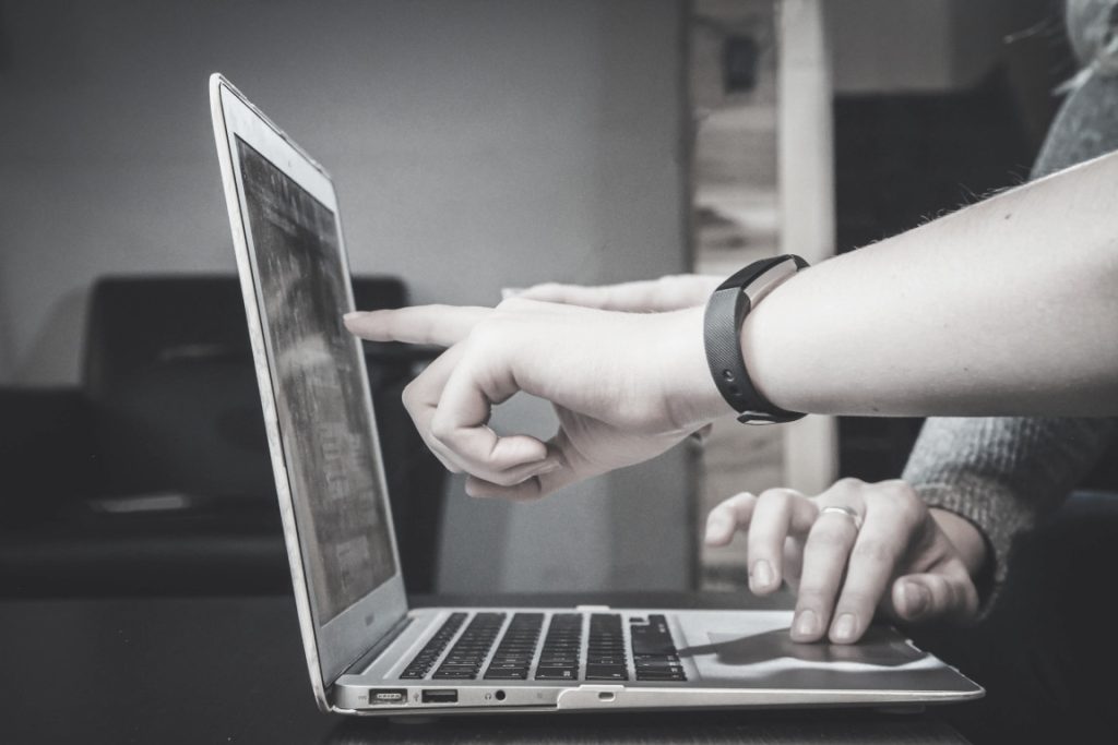 Someone pointing to a laptop screen whilst working with someone else